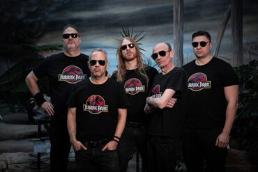 Vorax Death-Metal Band in dunkler Studio-Atmosphäre mit Jurassic Park T-Shirts.