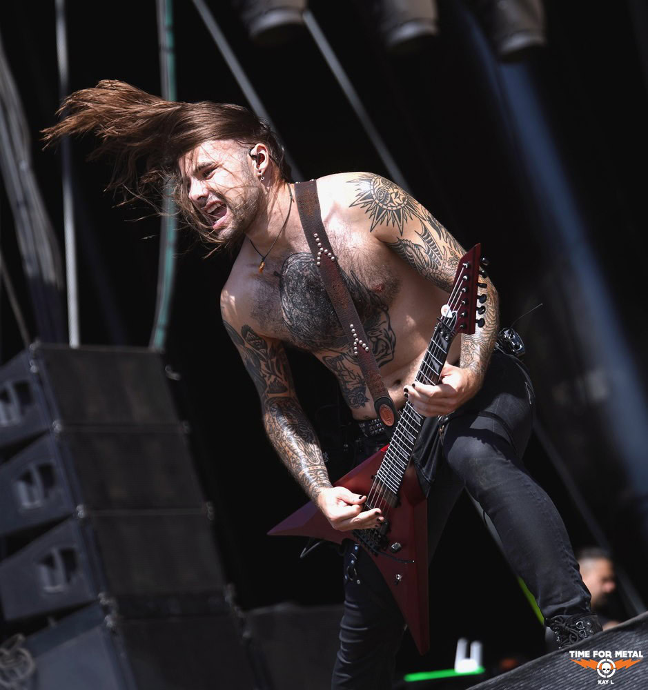Metal-Gitarrist mit langen Haaren und Tattoos beim Live-Auftritt.