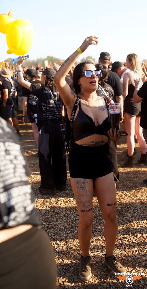 Frau mit Tattoos, Sonnenbrille und Getränk beim Metal Festival.