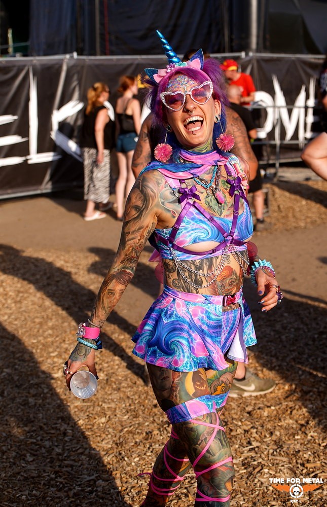Frau in bunter Fantasie-Outfit mit Einhorn-Horn und Tattoos bei Metal Festival.