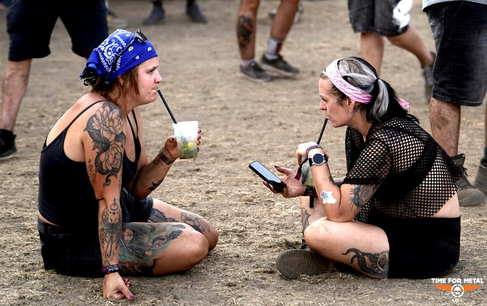 Zwei Frauen sitzen auf dem Boden bei einem Metal-Festival, trinken und chatten.