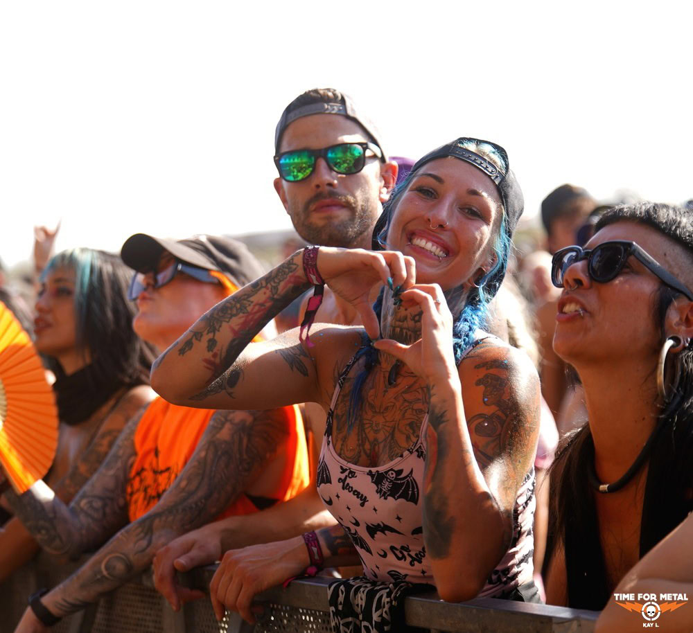 Fans beim Metal Festival mit Tattoos, Sonnenbrillen und Handzeichen.